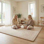 To kvinder sidder på Bella Tæppet 2.0 i beige i lys stue